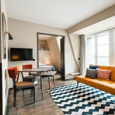 Sofa and seating area in suite at HENRI Hamburg Yellow sofa in front of a window and table with two chairs