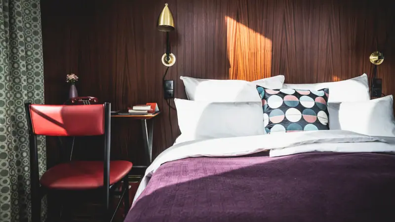 Rooms & Suites Bed with pillows and a desk in front of it in the hotel room.