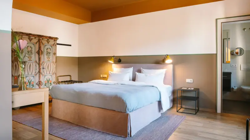 Hotel rooms at the HENRI Garmisch-Partenkirchen A hotel room at the HENRI Garmisch-Partenkirchen with a large cosy bed, an old wardrobe and a door to the adjoining bathroom.