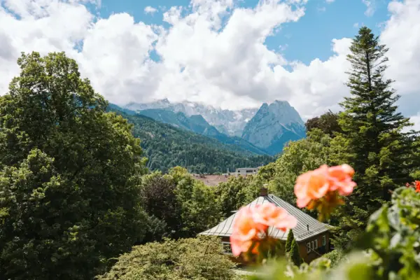 Outlook HENRI Garmisch-Partenkirchen View from the balcony of the HENRI Hotel Garmisch-Partenkirchen with flowers and mountains in the background.