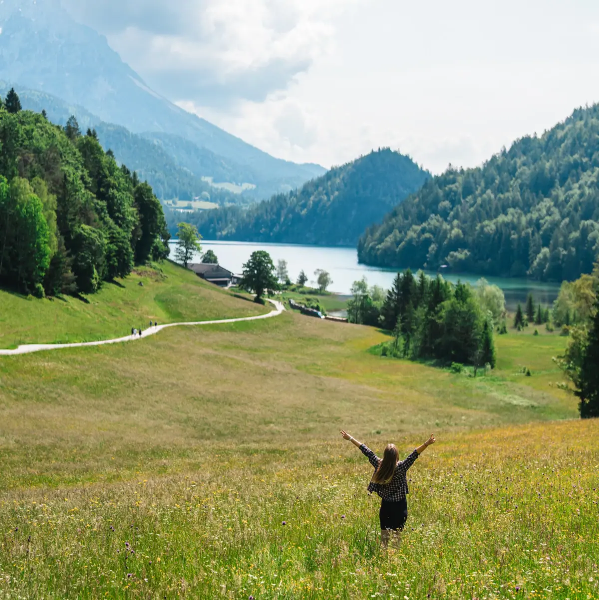 Woman stands on the alpine meadows and looks out over the lake and the mountains.
