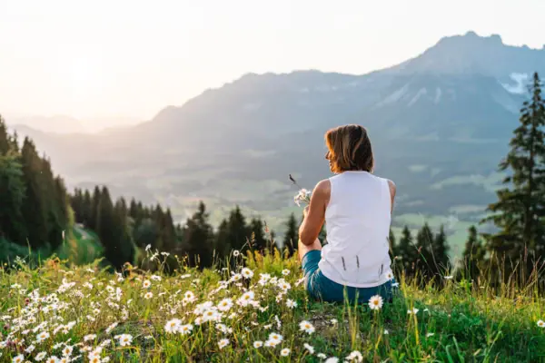 Woman sitting in the mountains A woman sits on a hill with flowers.