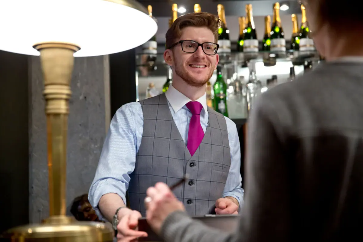Receptionist HENRI Hotel A man in a waistcoat and tie is standing at a reception desk.