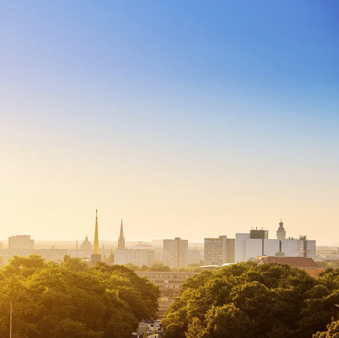 Leipzig City skyline with trees in the foreground and clear sky in the background.