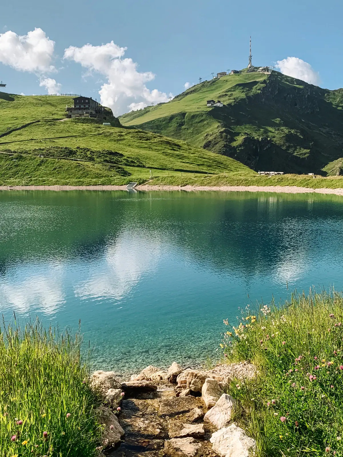 crystal-blue lake Body of water with hill and building in the background.