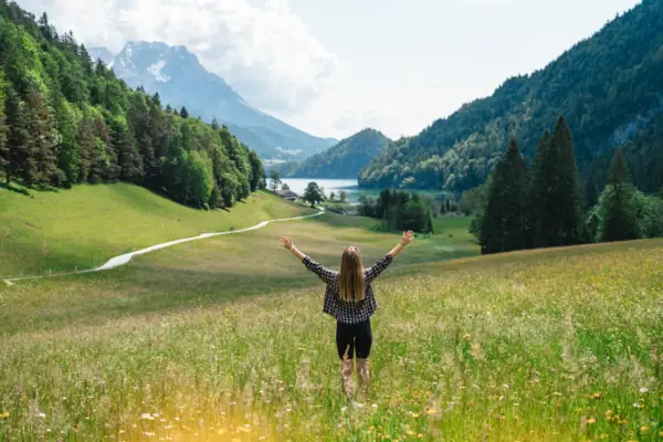 Mountain joy A woman stands in a field with her arms raised.