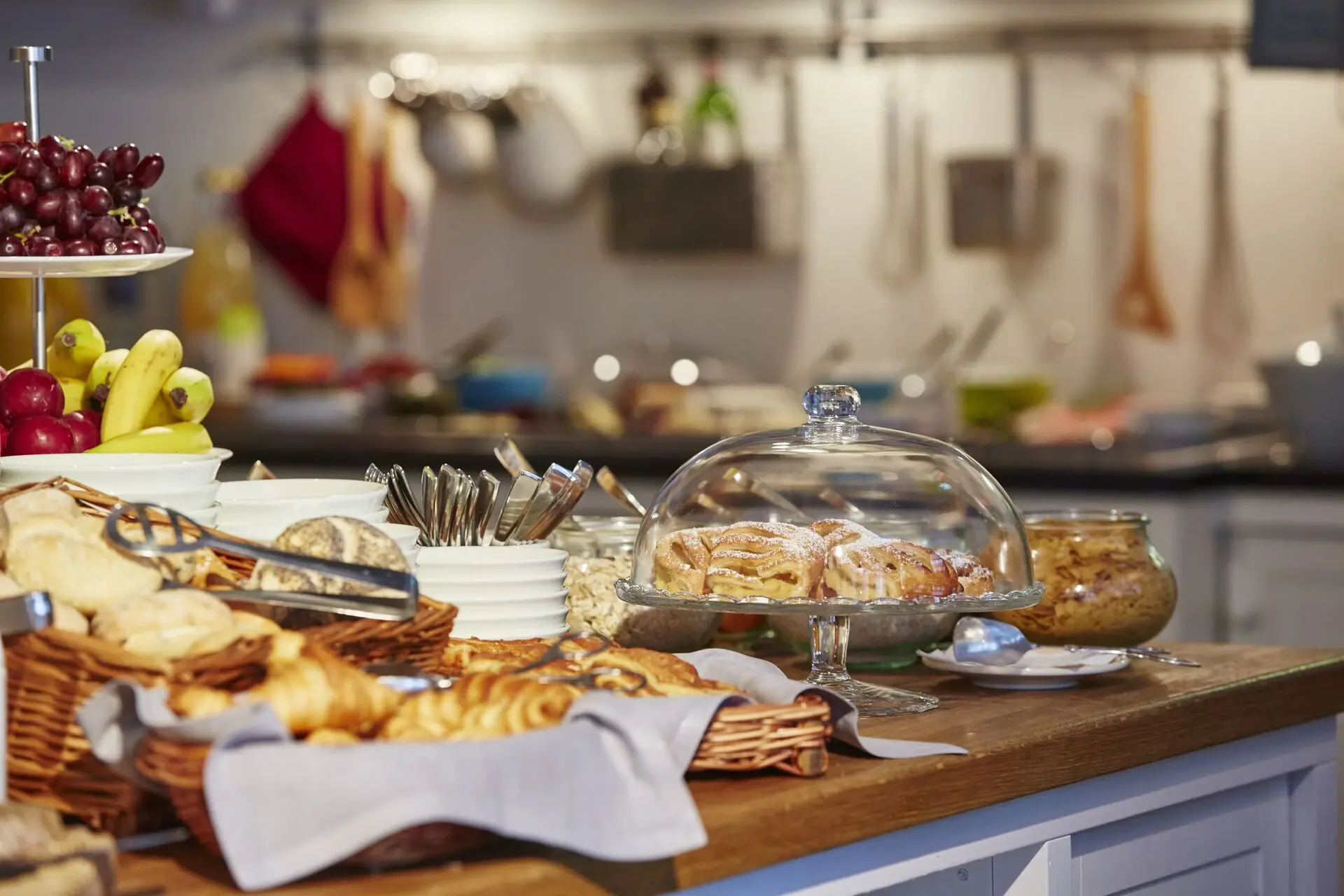 Breakfast buffet at the HENRI Hotel Hamburg Kitchen island with bread rolls, croissants and fruit.