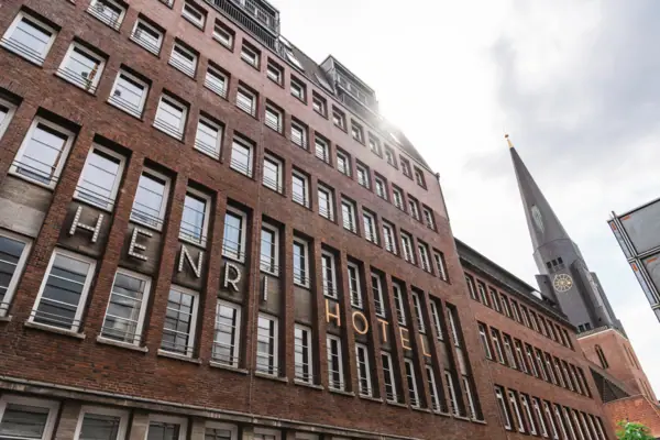 Exterior facade of the HENRI Hotel Hamburg A building with a high tower and windows against a cloudy sky.