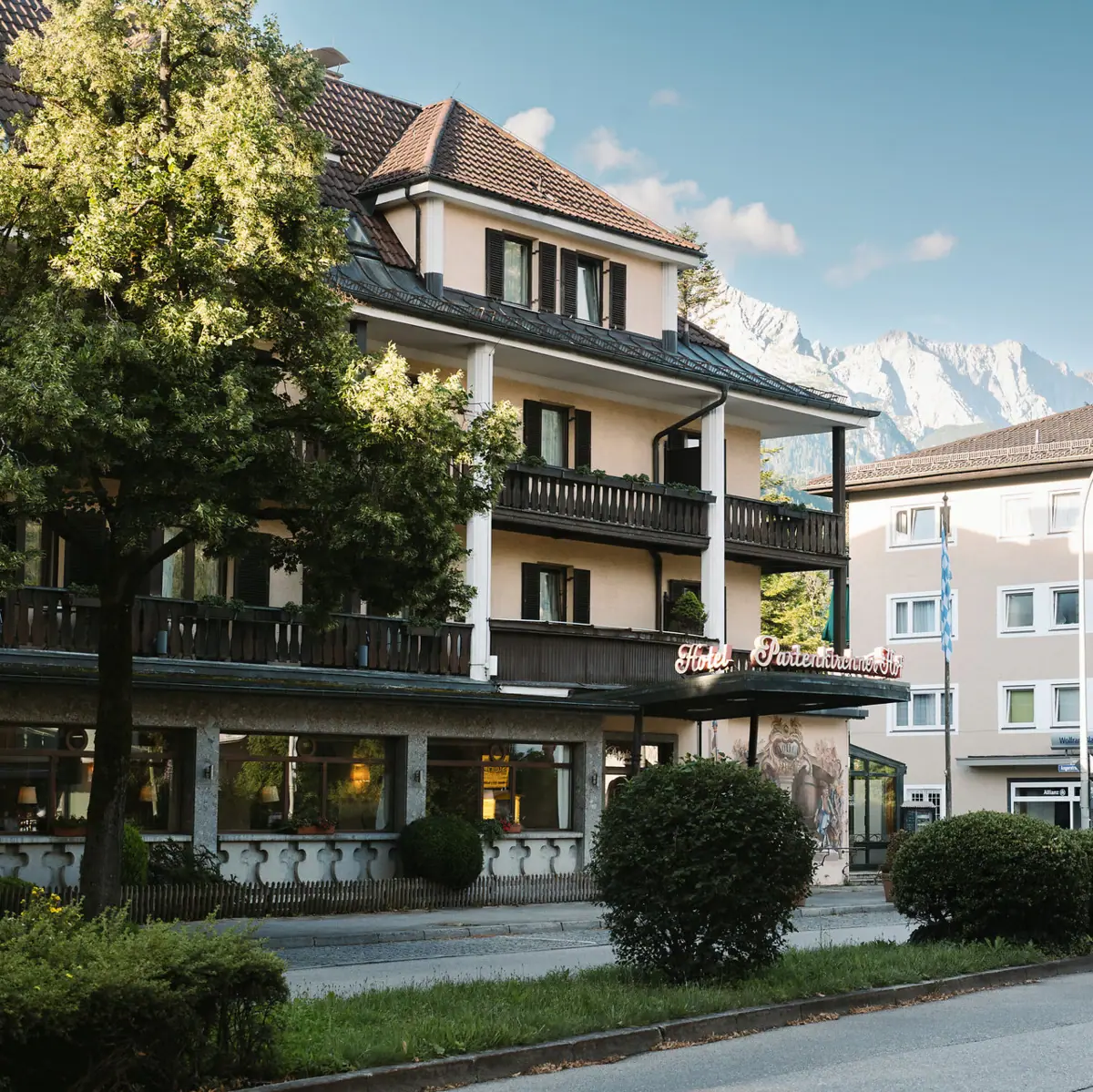 HENRI Hotel Garmisch-Partenkirchen The HENRI Hotel in Garmisch-Partenlkirchen with trees by the roadside and mountains in the background.