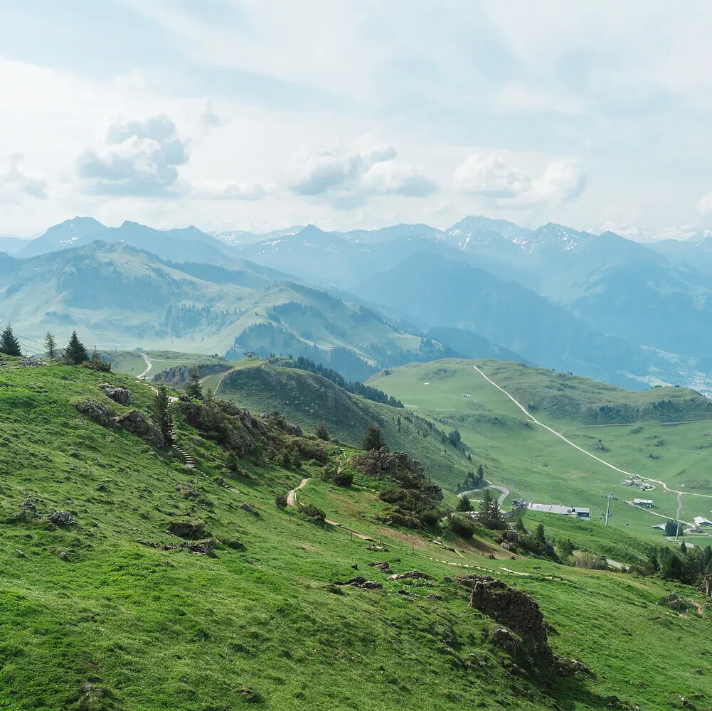 Kitzbühler Horn Green hills with a road and mountains in the background.
