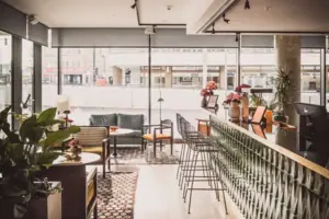 HENRI Düsseldorf A room with a bar and chairs, featuring furniture and houseplants.