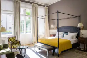 HENRI Berlin Zimmer A room featuring a neatly made bed with pillows and a nearby chair.