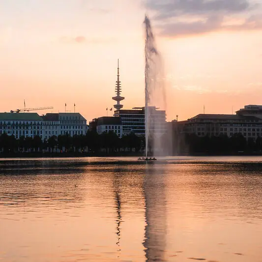 Alster Fountain in a body of water with buildings in the background.
