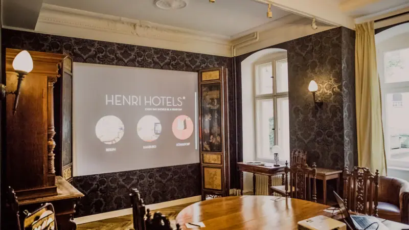 HENRI Men's room A room with a projection screen and wooden furniture.