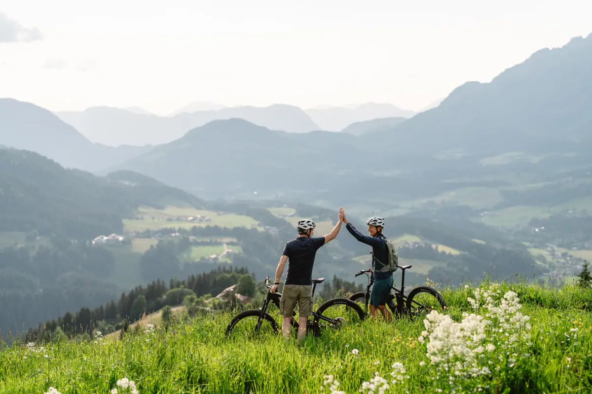 Two people with bicycles on a hill outside.