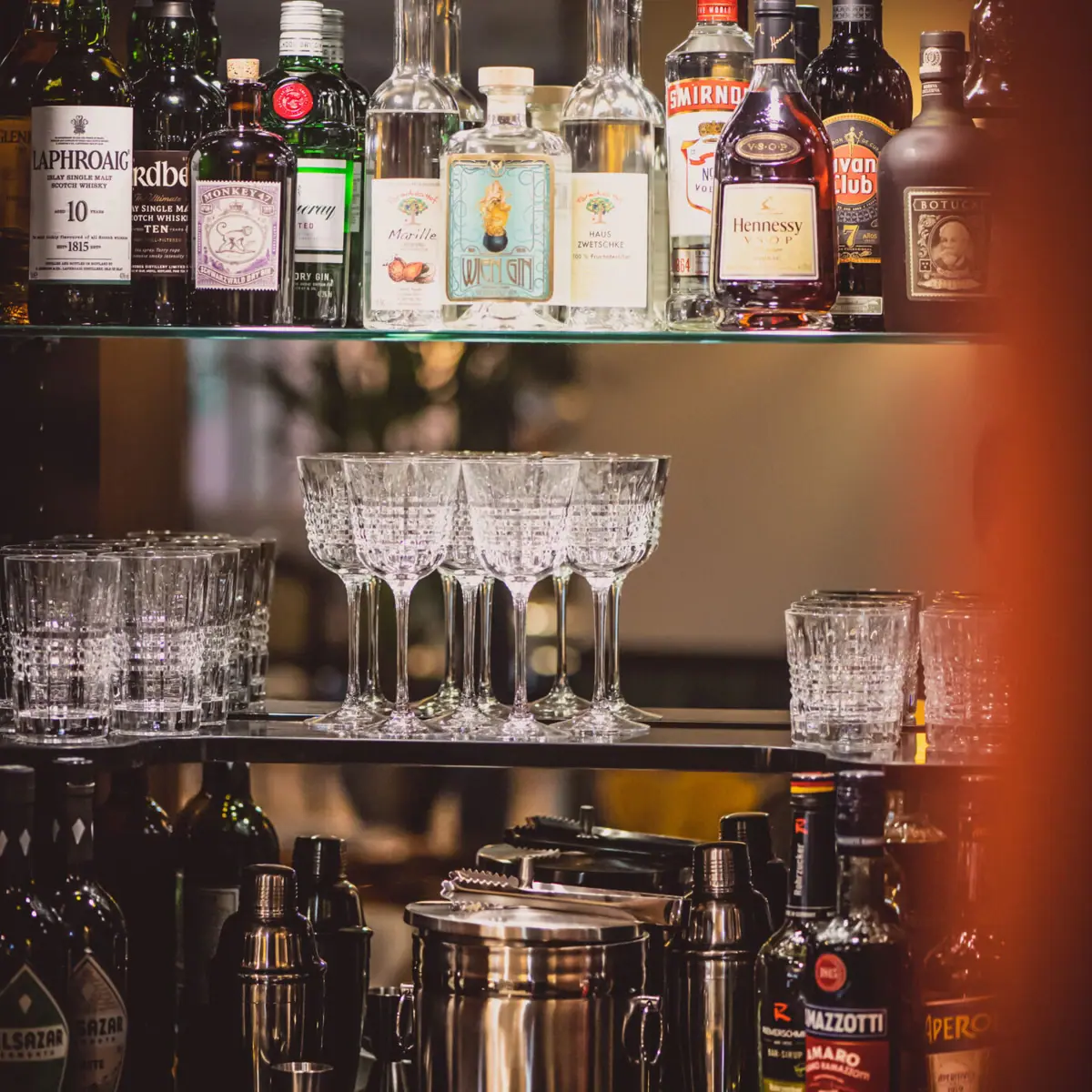 HENRI Bar Shelf with glasses and bottles of alcoholic drinks in a bar.