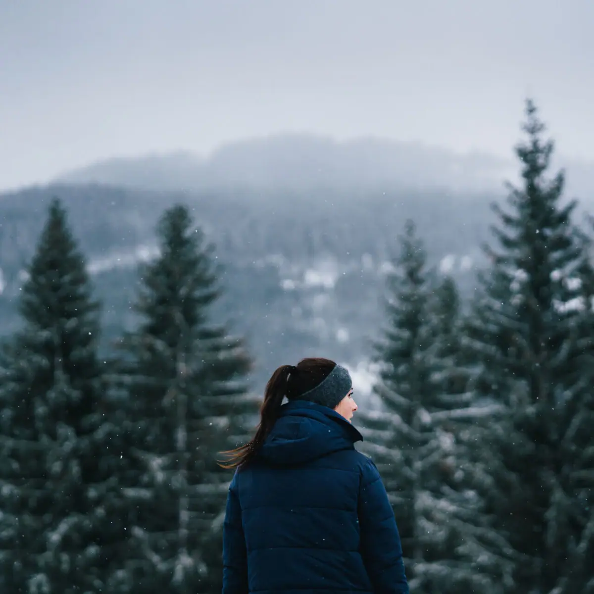 A woman stands in front of snow-covered trees.