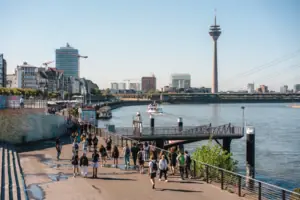 Düsseldorf A group of people walking on a path near a lake with a clear sky.