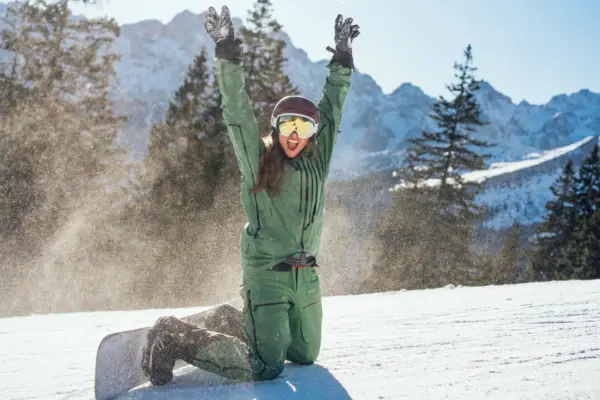 Snowboarder Garmisch-Partenkirchen A woman in winter clothing kneels in the snow with her hands raised.