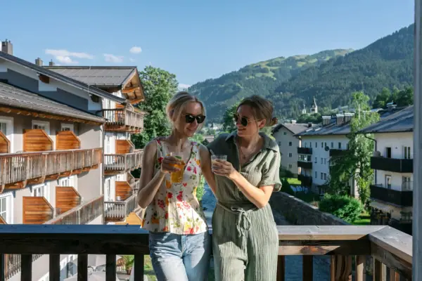 Kitzbühel Two women stand on a balcony with a view of mountains and trees.