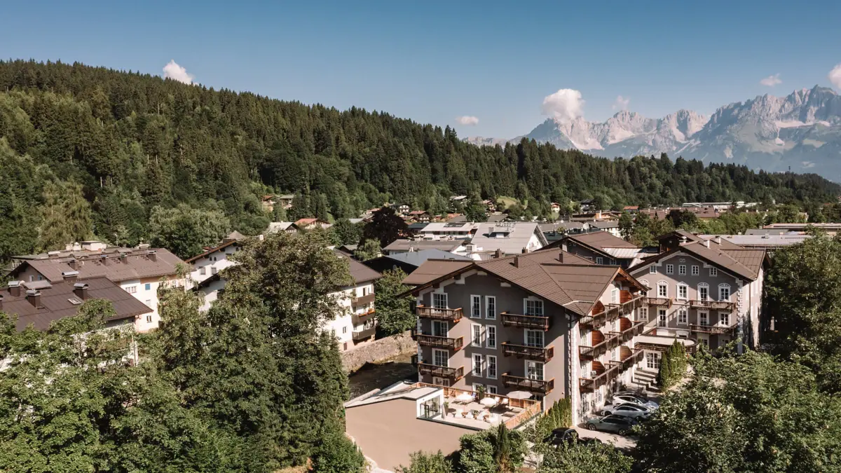 HENRI Hotel Kitzbühel in front of an Alpine panorama A group of buildings with trees and mountains in the background.