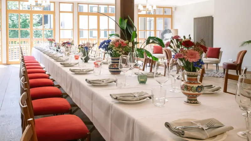 HENRI Kitzbühel event room A long table with white tablecloths and red chairs.