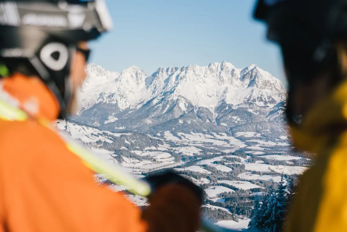 A group of people on a ski slope looking at a snow-covered mountain.