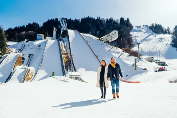 Olympic ski jump Garmisch-Partenkirchen A man and a woman are walking in the snow in front of a large ski jump.
