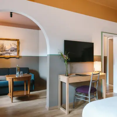 Suite at the HENRI Garmisch-Partenkirchen A suite at the HENRI Garmisch-Partenkirchen with a separate living and sleeping area, a desk and a TV on the wall,