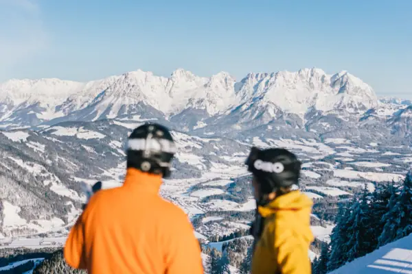 Tyrolean Alps in the snow Two people wearing helmets look out over snow-covered mountains.