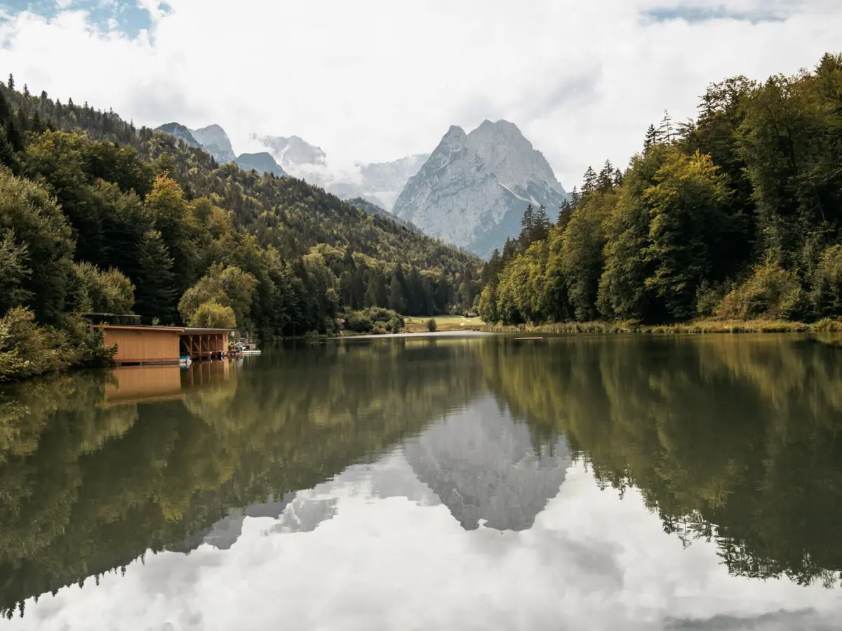 Riessersee A lake with a hut and mountains in the background.