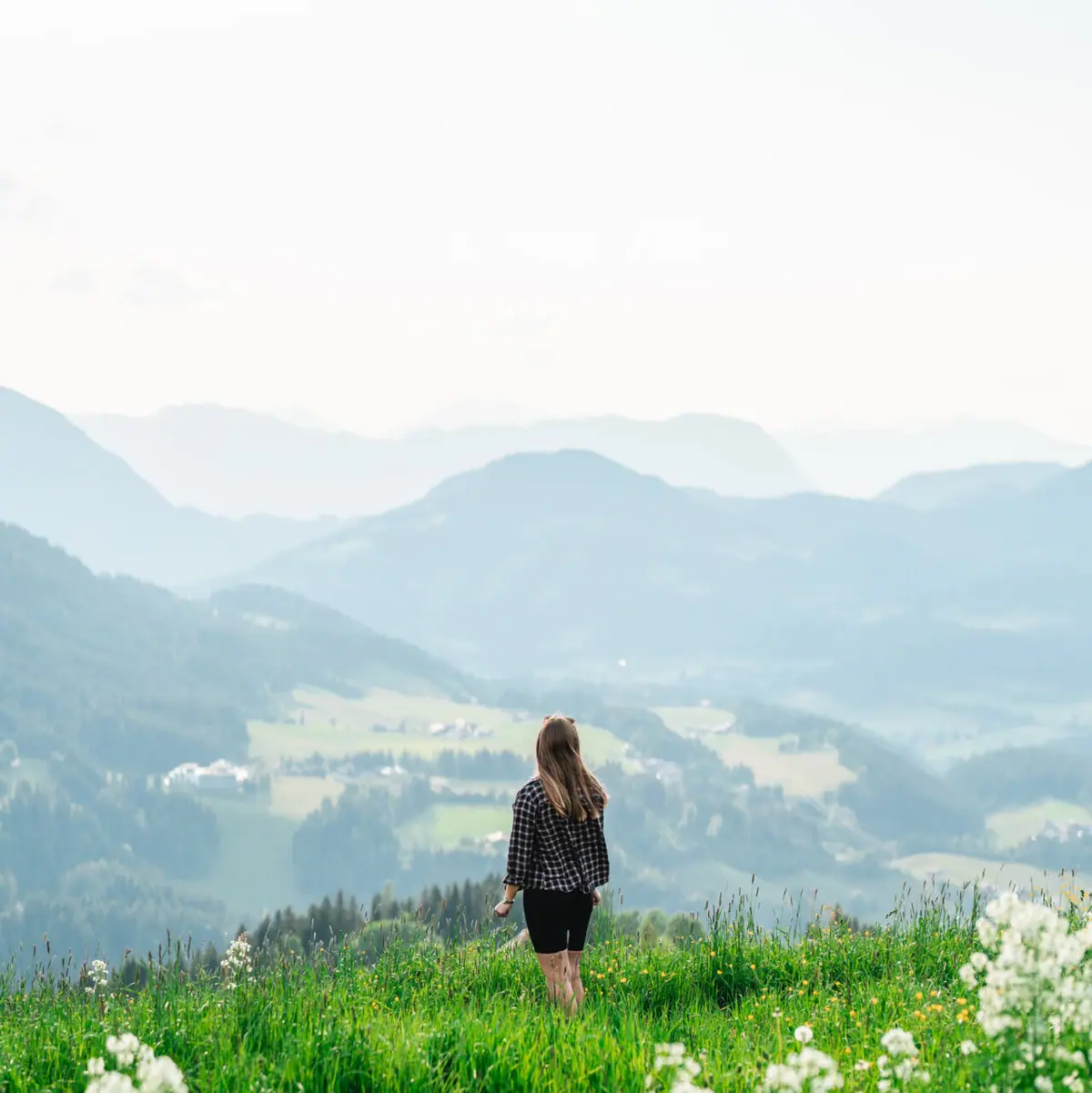 Woman standing in the mountains A woman stands on a grassy hill with mountains in the background.