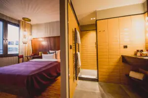 S-Studio HENRI Düsseldorf The S-Studio in the HENRI Hotel Düsseldorf with a bed and an adjoining bathroom with a washbasin and shower.