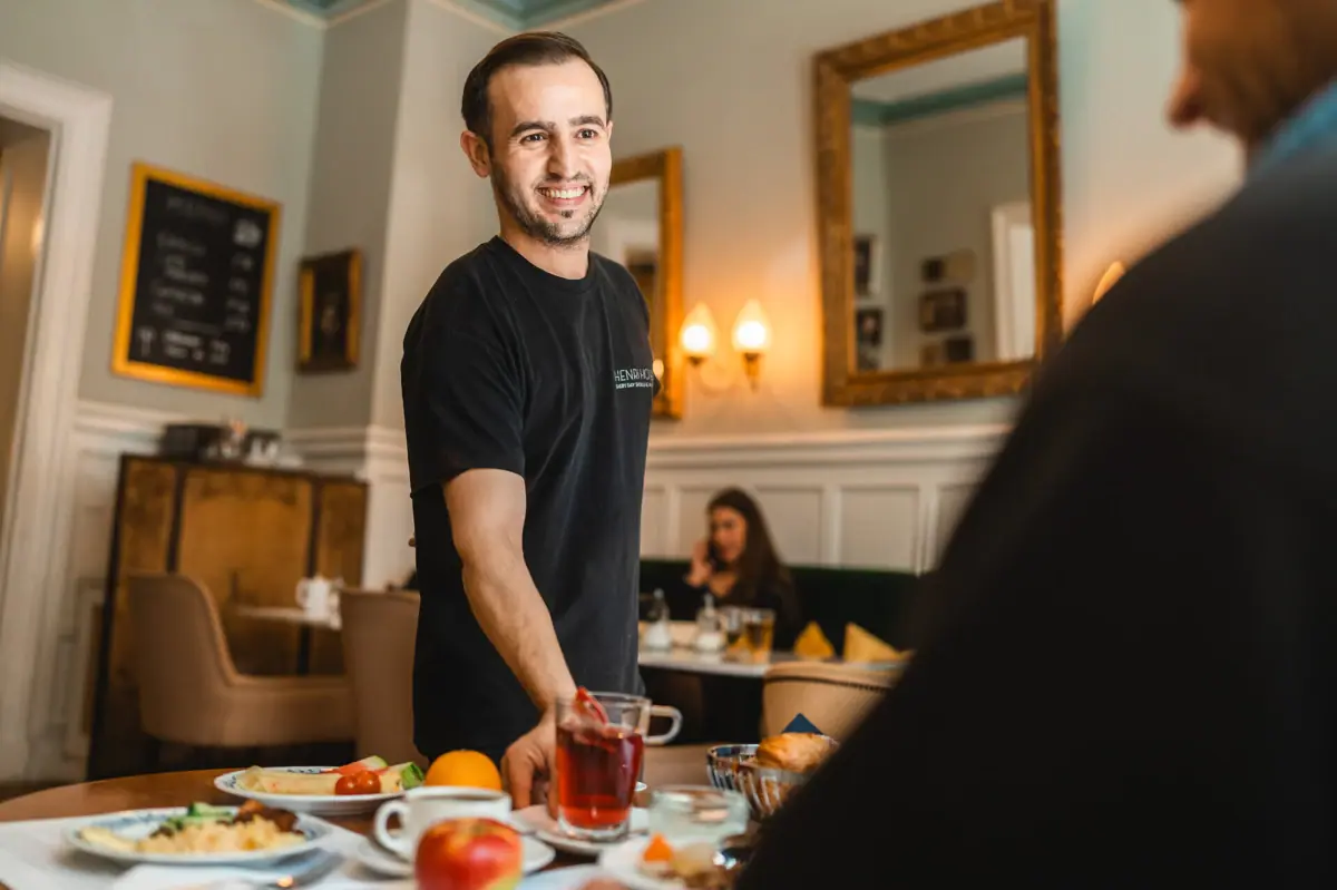 HENRI Berlin A man smiles at a table with food.