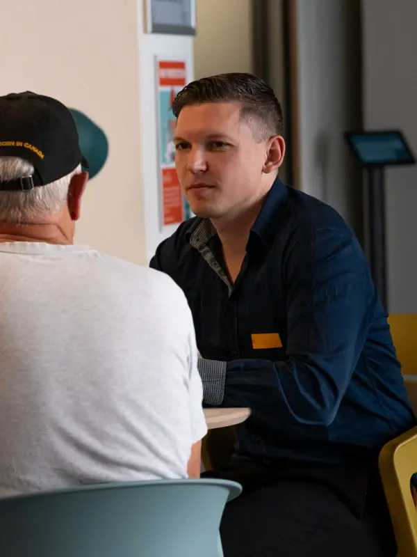 Coworking Space A man is sitting at a table with another man in a white shirt.