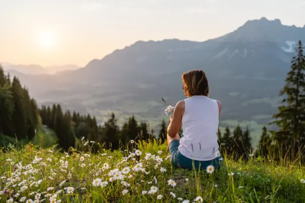 View of the Alpine panorama A woman sits on a hill with flowers.