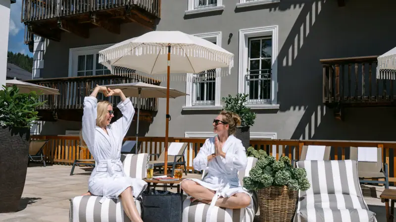 Sun terrace at the HENRI Hotel Kitzbühel Two women in bathrobes sit on a terrace.