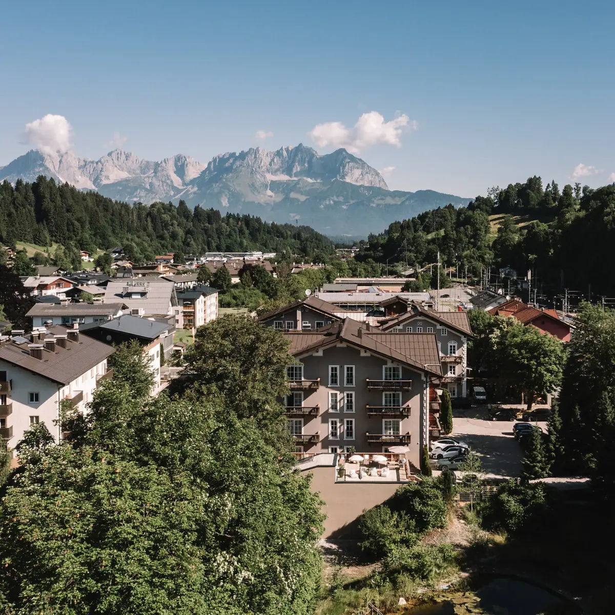 HENRI Hotel Kitzbühel in front of the Alps Small town with trees and mountains in the background.