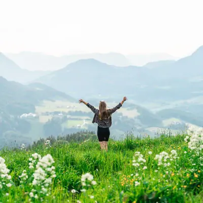 Alps panorama A woman stands in a field of flowers with her arms raised.