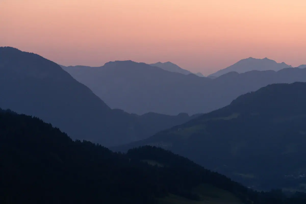 A mountain range with trees and a pink sky.