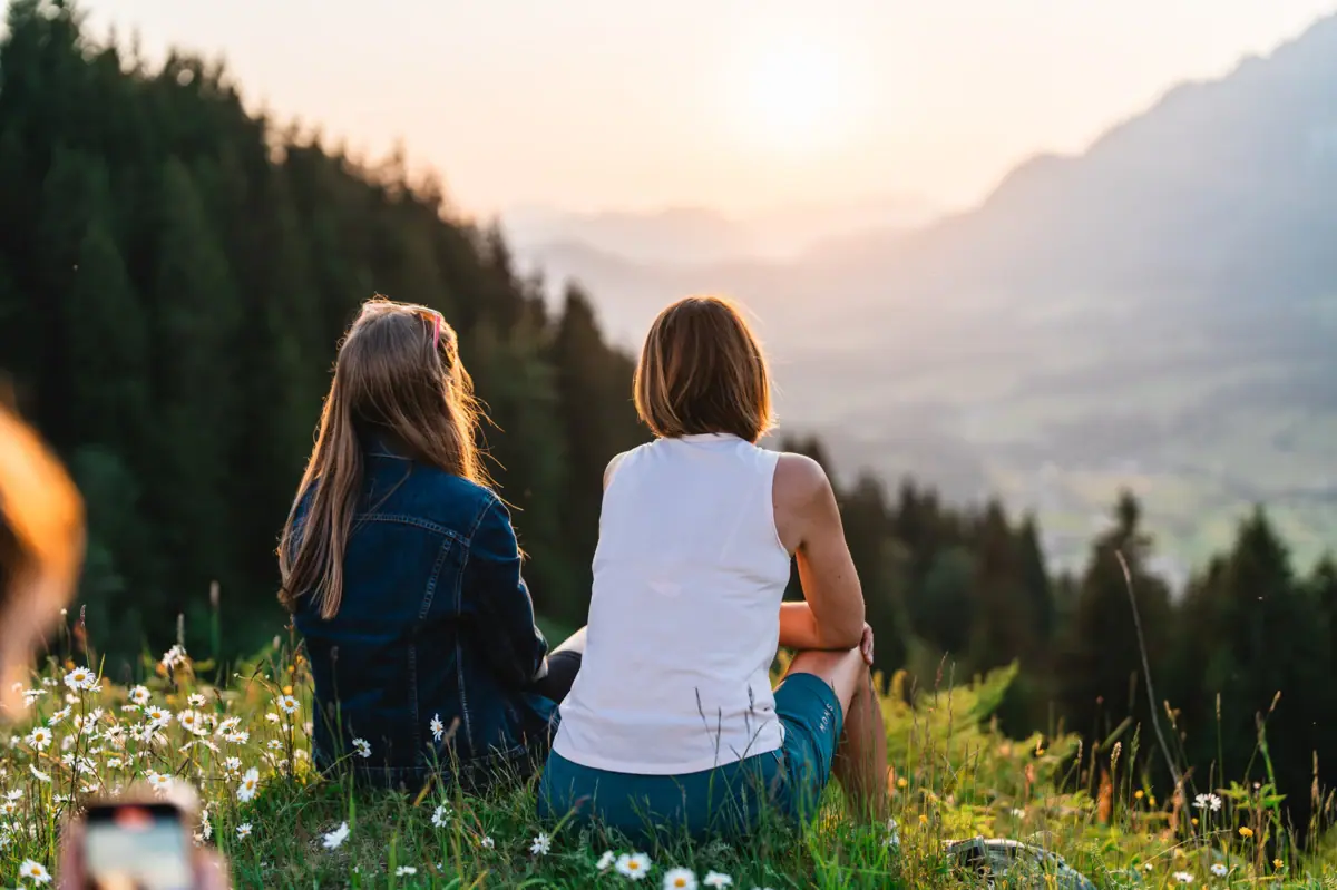 View of the Kitzbühel Alps Two women sit on a hill and watch the sunset.