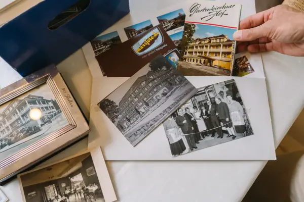 History of Reindel HENRI Garmisch-partenkirchen One hand holds a few old postcards and photos.