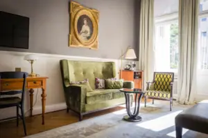 HENRI Hotel Berlin Zimmer Kurfürstendamm Klassisches Hotelzimmer im Gründerzeit-Stil mit einem grünen Samtsofa, antikem Schreibtisch und herrschaftlichem Porträtgemälde an der Wand.