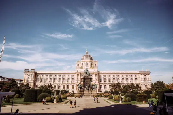 Museum building in Vienna Large building with a statue in front of it, surrounded by trees and sky in the background.