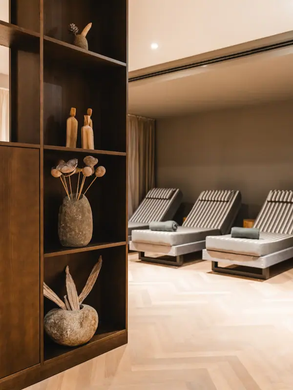 HENRI Kitzbühel relaxation area A room with chairs and a shelf with vases and flowers.